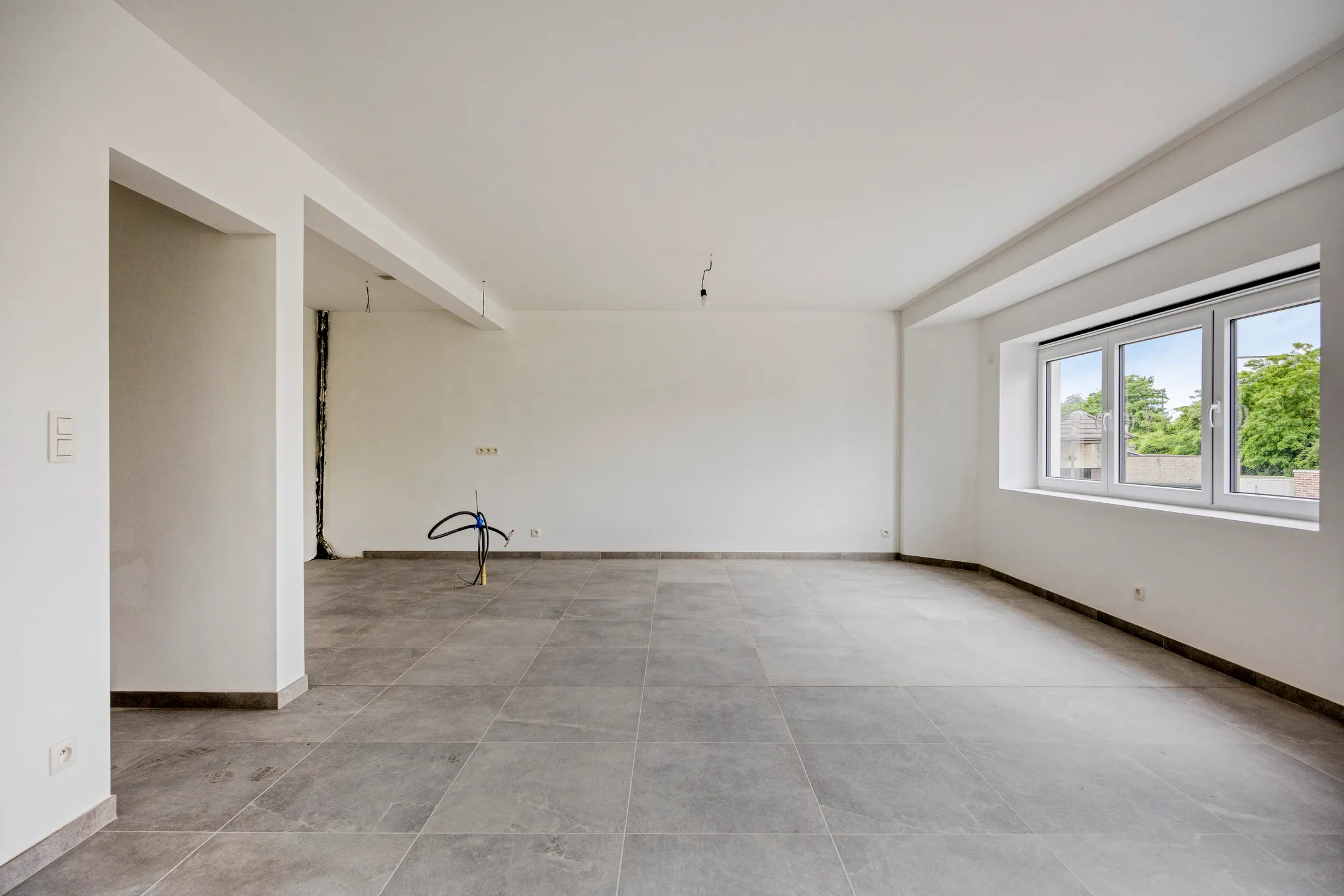 Woonkamer met groot raam en tegelvloer, open plan