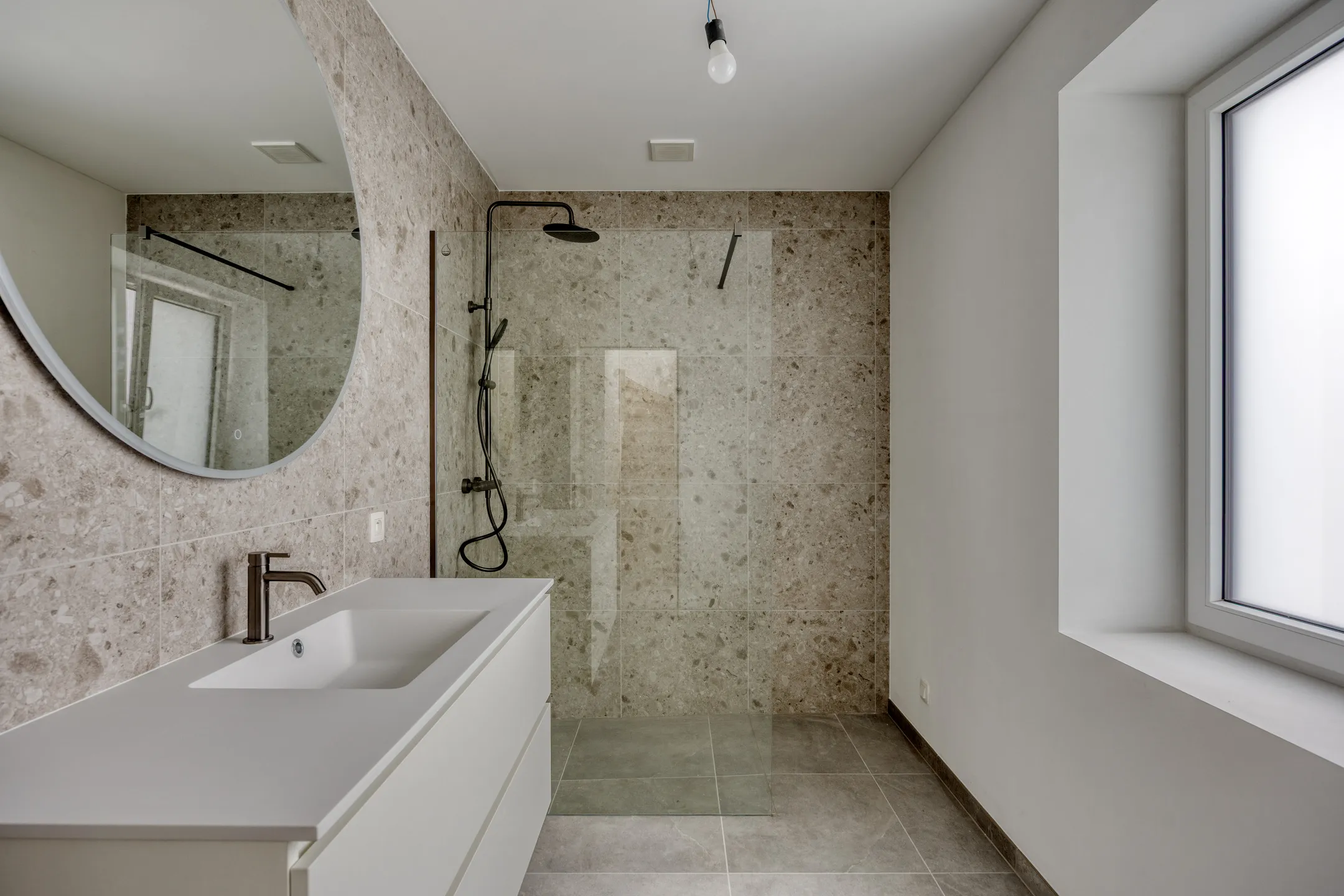 Badkamer met inloopdouche, meubel en ronde spiegel