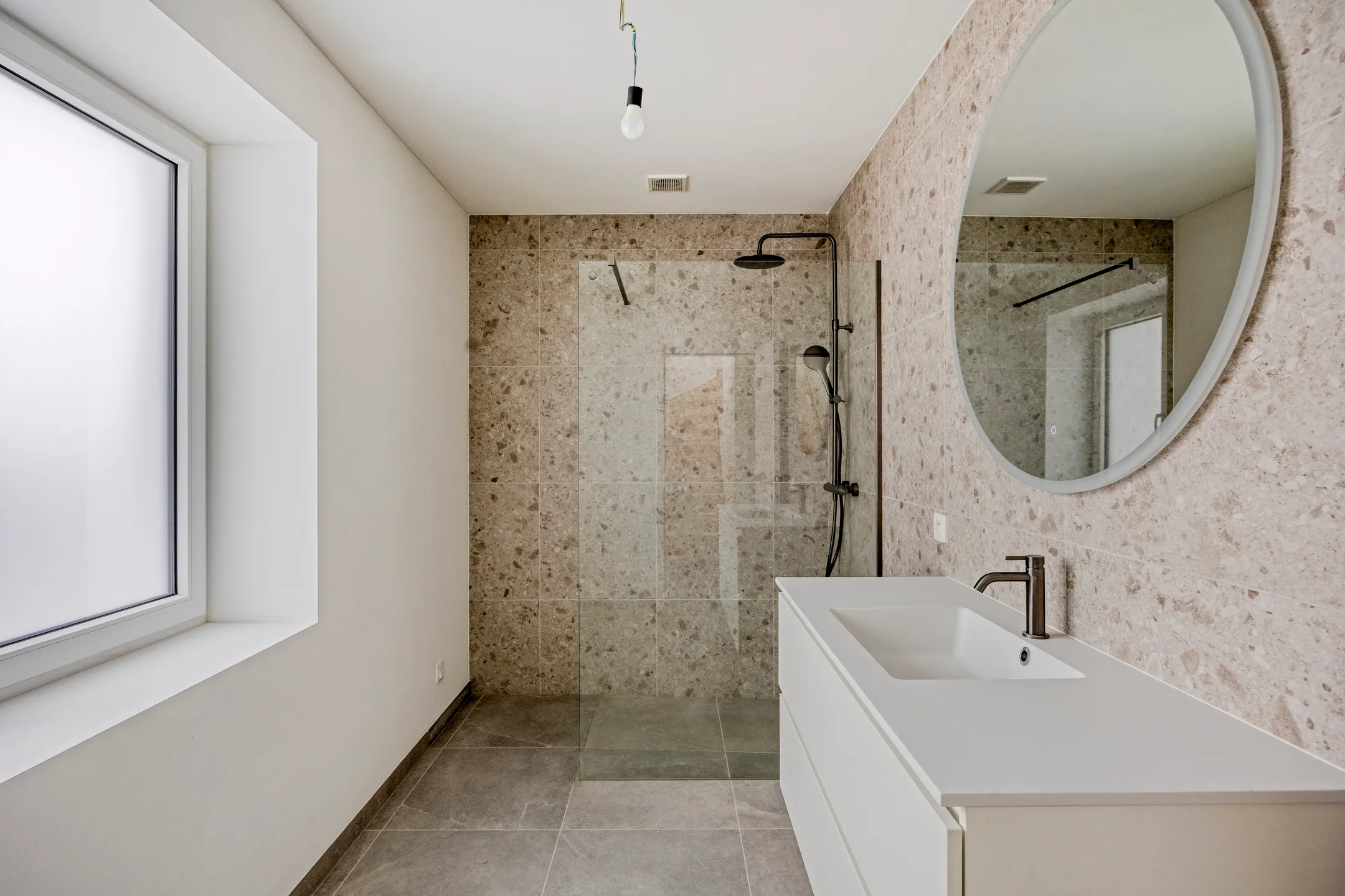Badkamer met inloopdouche, ronde spiegel en meubel