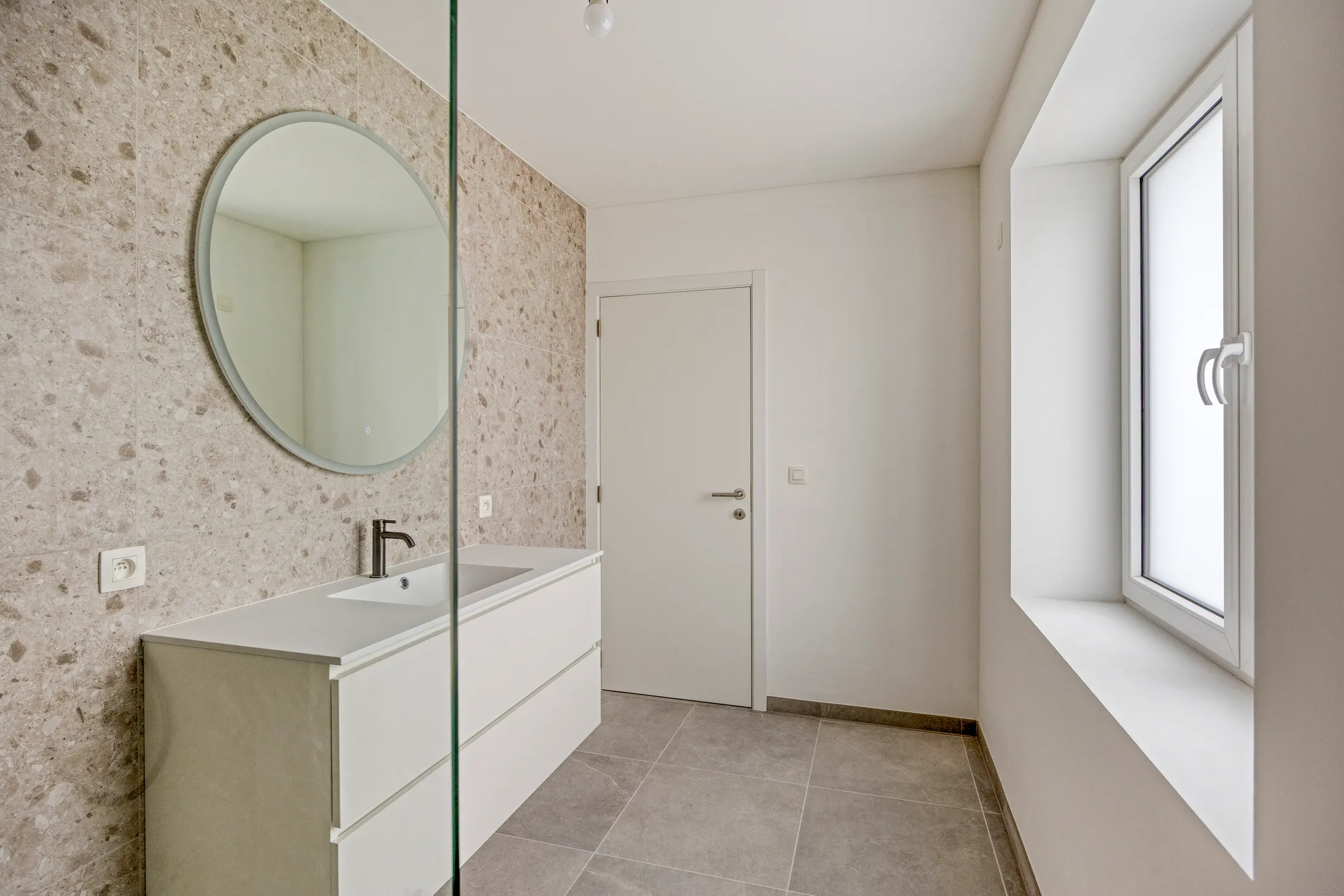 Badkamer met meubel, ronde spiegel en matglas raam