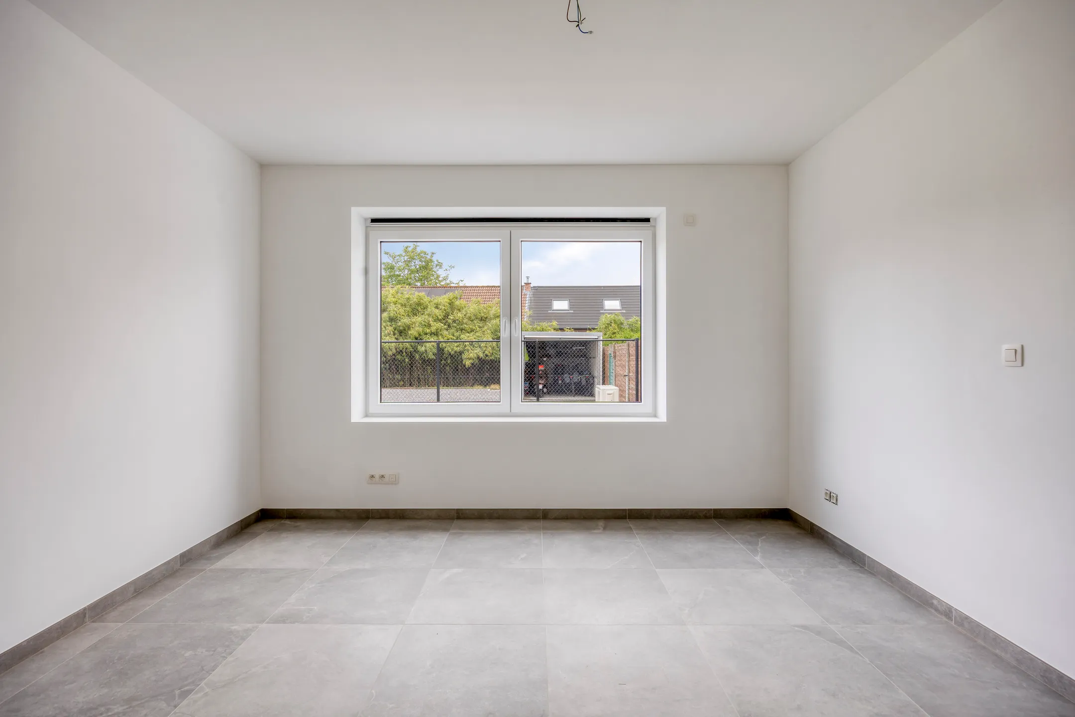 Slaapkamer met raam en zicht op de buurwoningen