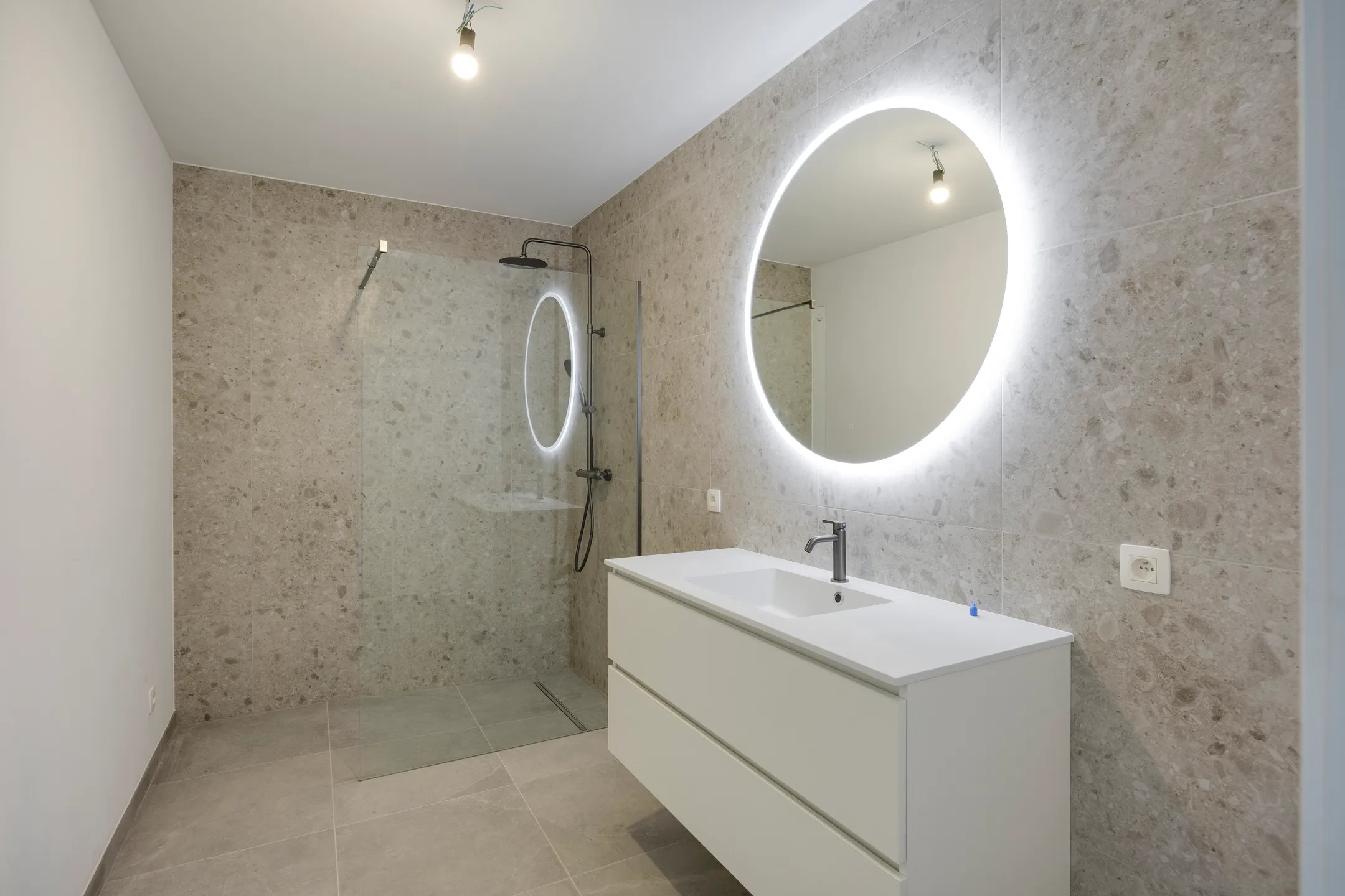 Badkamer met inloopdouche, meubel en ronde verlichte spiegel