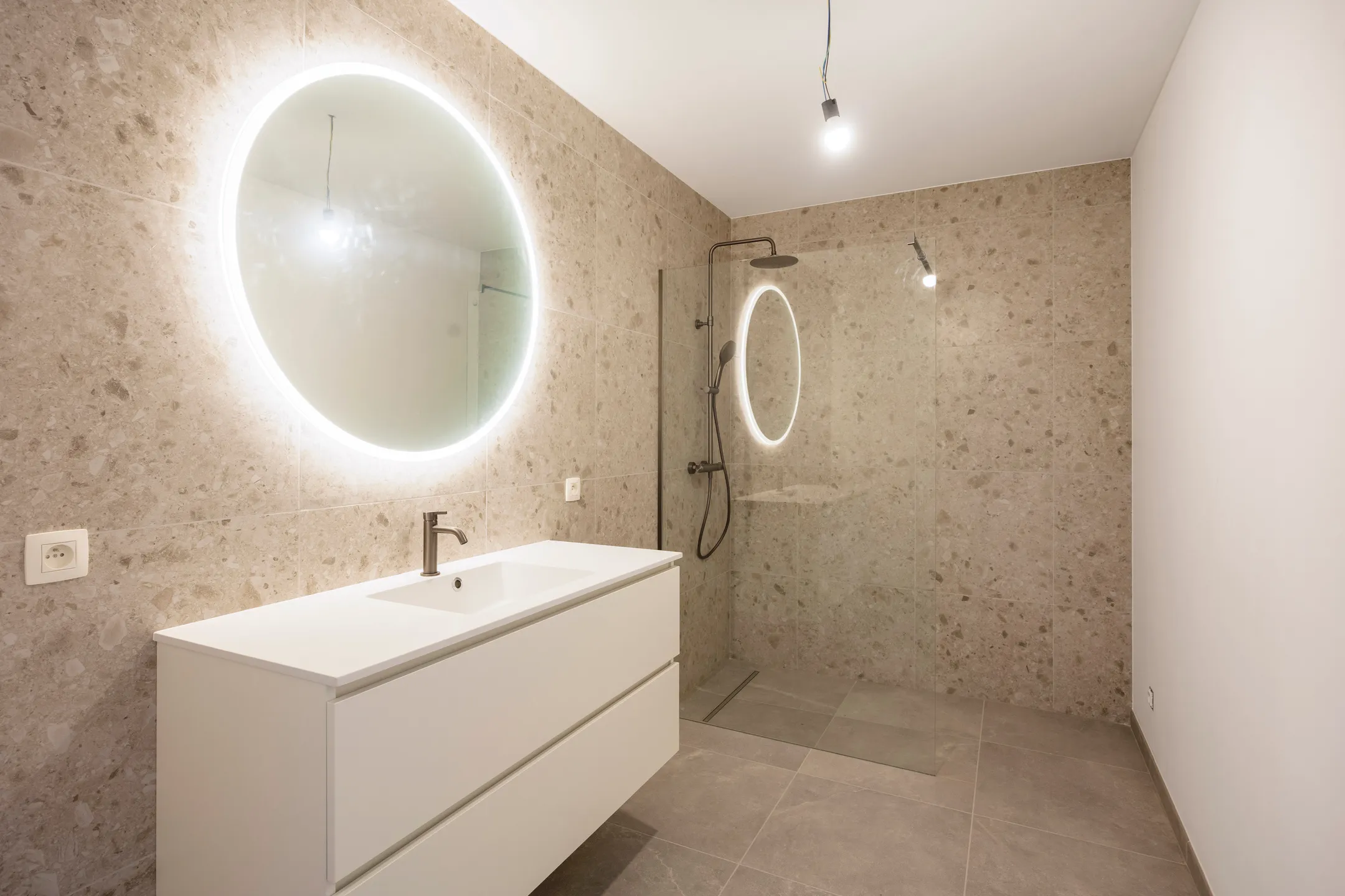 Badkamer met meubel, ronde verlichte spiegel en inloopdouche