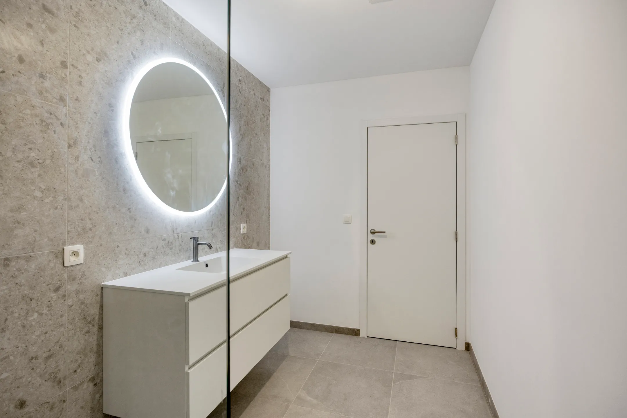 Badkamer met meubel en ronde verlichte spiegel