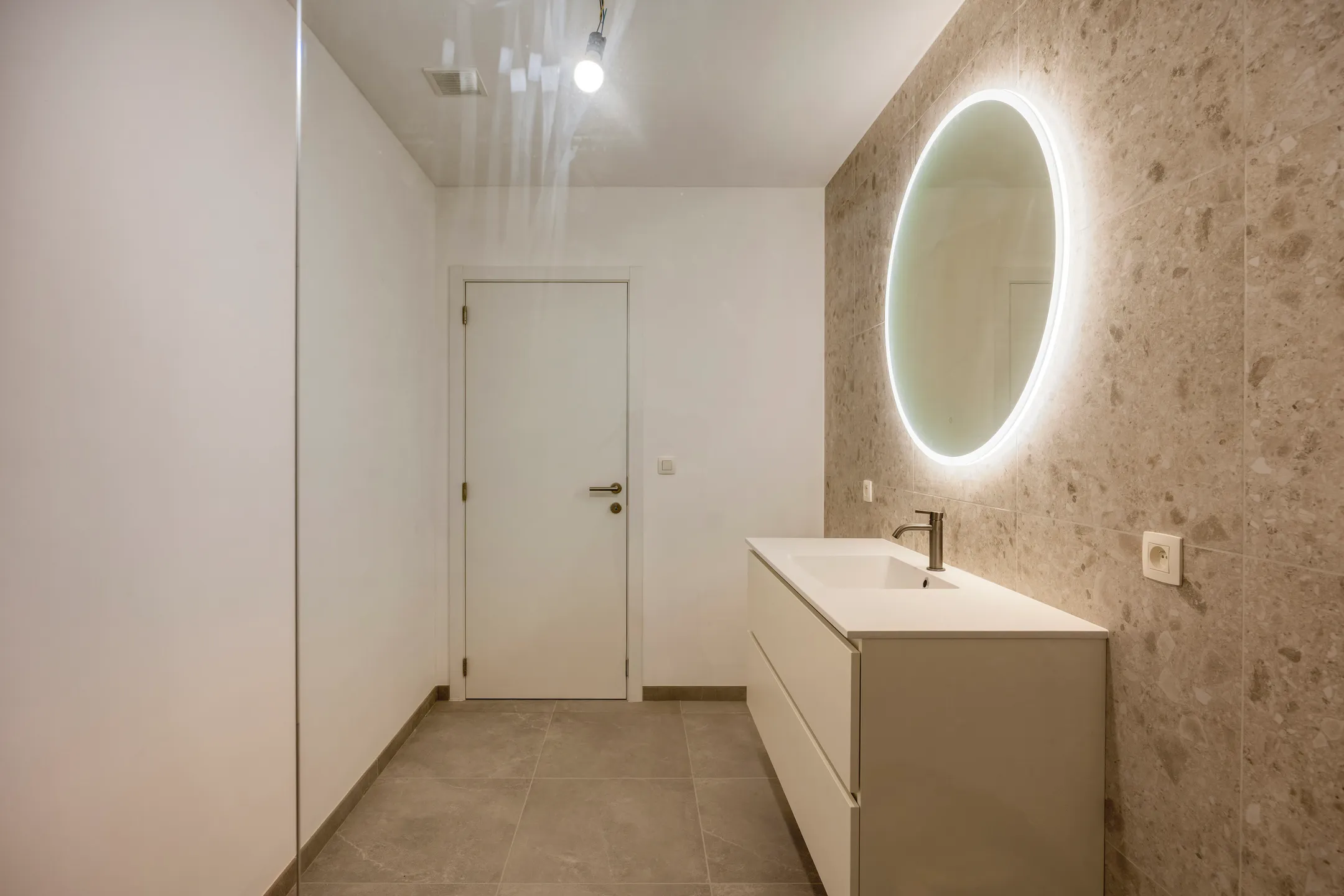 Badkamer met meubel, ronde spiegel en deur